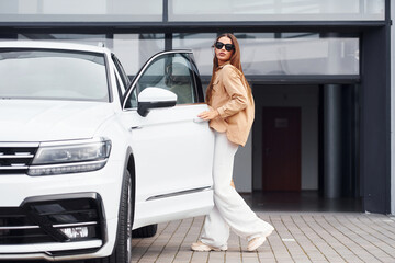 Outside near car. Fashionable beautiful young woman and her modern automobile
