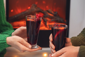 Couple with glasses of delicious mulled wine near fireplace