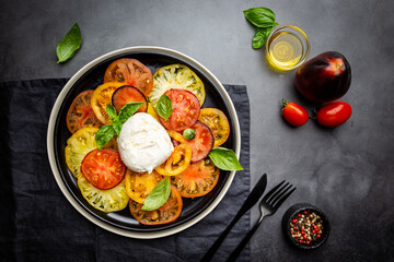 Delicious caprese salad with ripe colorful tomatoes and mozzarella cheese with fresh basil leaves. Italian food, top view