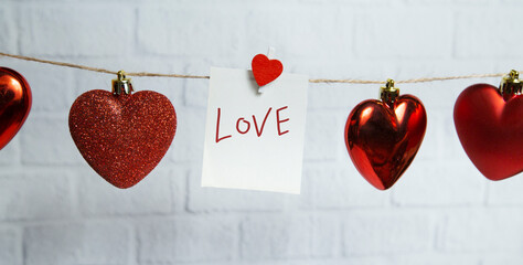 red hearts and white card hang on a thread on a white brick background