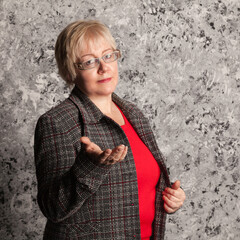Studio portrait of blonde mature woman with short haircut in purple woolen jacket on gray textured background
