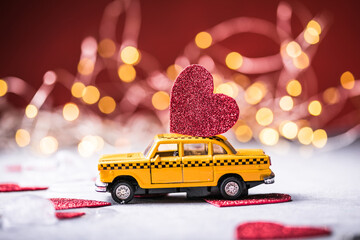 Red heart on toy yellow  taxi car on red background. Travel love concept with copy space.