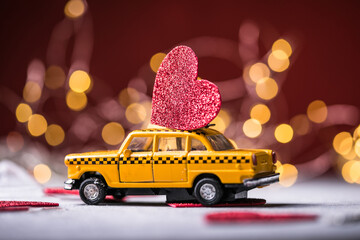 Red heart on toy yellow  taxi car on red background. Travel love concept with copy space. © Maria