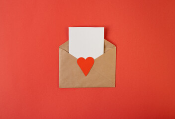 Craft envelope with blank white note mockup inside and Valentines hearts on red background. Flat lay, top view. Romantic love letter for Valentine's day concept.