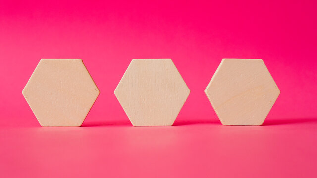 Three wooden hexagonal shapes stand against a background of pink paper