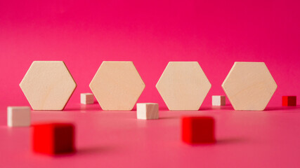 four wooden hexagonal shapes  stand against a background of pink paper with some cubes in red and...