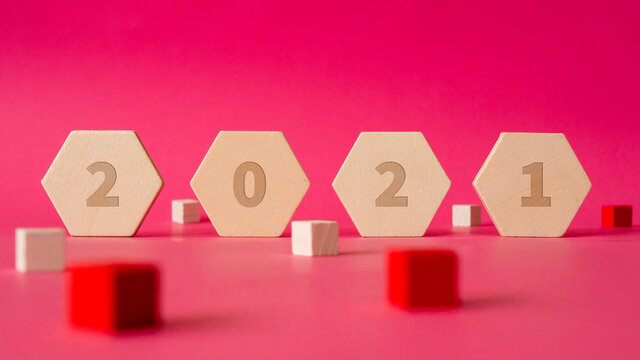 four wooden hexagonal shapes with numbers of new year 2021 stand against a background of pink paper with some cubes in red and white arround