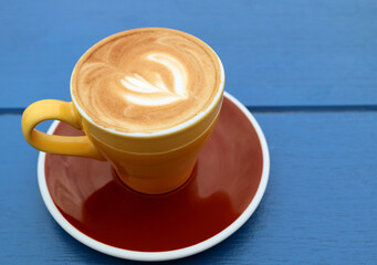 Closeup of cappuccino coffee in yellow brown cup isolated on blue wooden table