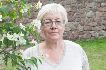 Mature blonde short haired woman in linen clothes near jasmine flowers