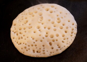 A white pancake with bubbles on the hot stove