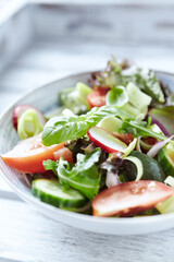 Salad with feta cheese, radish, rocket, green olives, tomatoes, cucumber and fresh basil. Bright wooden background. Close up.