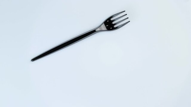 Black plastic disposable fork rotates in a circle on a white background.