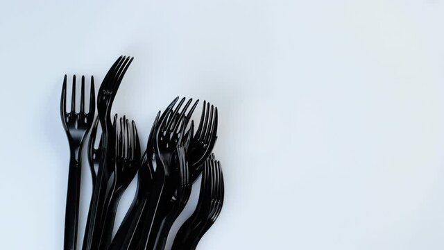 Many black plastic disposable forks spin on a white background.