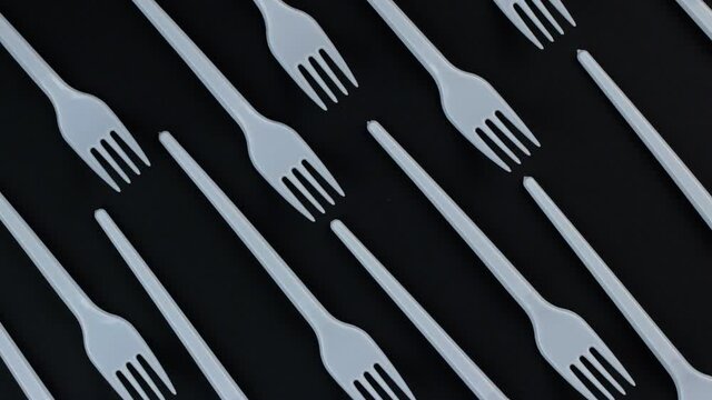 Eco concept. Plastic disposable forks stacked in rows on a black background rotate in a circle. Pattern