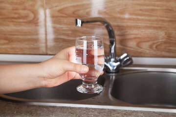 Woman pouring a glass of filling water from a kitchen faucet.