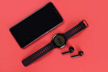 Gadgets on a red background: smartwatch, Bluetooth headphones and phone