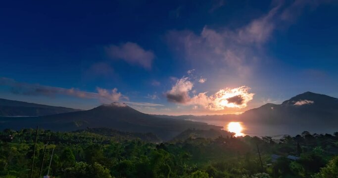 Timelapse of sunrise with view on volcanoes and lake. Clouds are moving quick in blue sky, the sun is rising