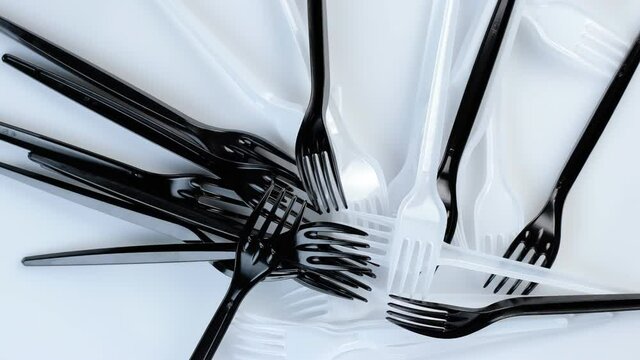 Many black plastic disposable forks spin on a white background.