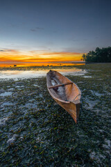 A wooden boat pulls up on the seaweed at dusk