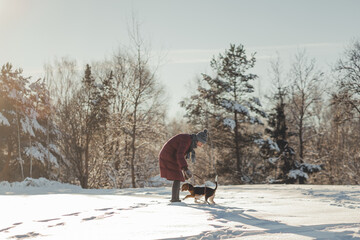Girl in a red down jacket on walk with purebred beagle puppy in winter park. 