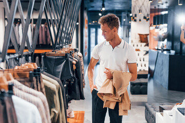 Fototapeta premium Looks for jacket. Young guy in modern store with new clothes. Elegant expensive wear for men