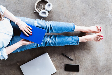 Girl in jeans sitting on the floor at home with a notebook, laptop, phone, pen and headphone