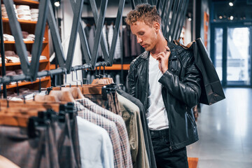 Big choice. Young guy in modern store with new clothes. Elegant expensive wear for men
