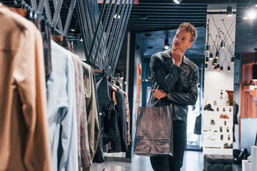 Big choice. Young guy in modern store with new clothes. Elegant expensive wear for men