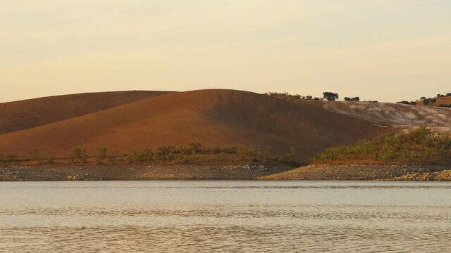 Desert like hill landscape with reflection on the water on a dam lake reservoir at sunset in Terena, Portugal