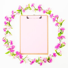 Flower frame of pink flowers and clipboard with pink paper on white background. Flat lay