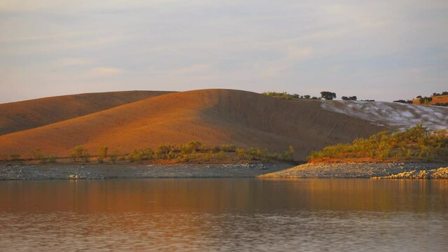 Desert like hill landscape with reflection on the water on a dam lake reservoir at sunset in Terena, Portugal