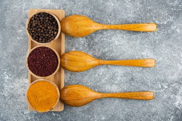 Different spices with wooden spoons on a gray background