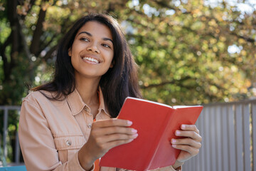 Portrait of beautiful smiling woman reading book, studying, learning language, sitting in park