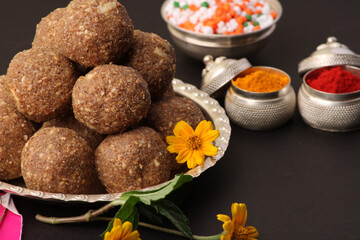 Til Gul OR Sweet Sesame Laddu with Kite model, haldi Kumkum and sugar crystals for Makar Sankranti festival over black background.