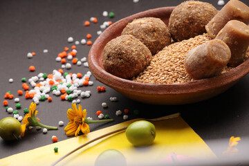 Til Gul OR Sweet Sesame Laddu with Kite model, haldi Kumkum and sugar crystals for Makar Sankranti festival over black background.