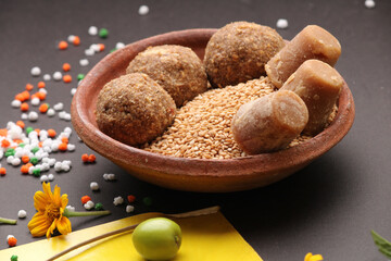 Til Gul OR Sweet Sesame Laddu with Kite model, haldi Kumkum and sugar crystals for Makar Sankranti festival over black background.