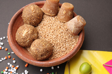 Til Gul OR Sweet Sesame Laddu with Kite model, haldi Kumkum and sugar crystals for Makar Sankranti festival over black background.