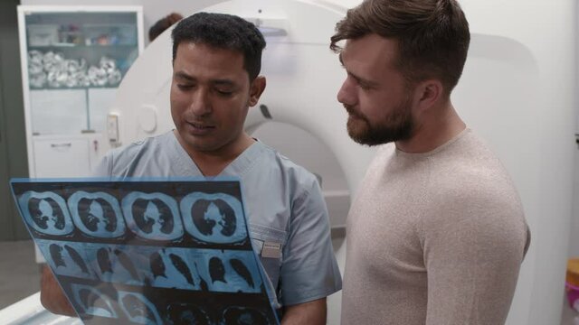 Medium shot with slowmo of Arab male doctor holding CT scan of lungs and talking to patient