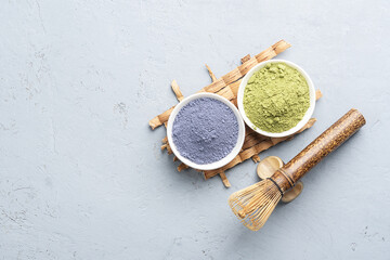 Bowls of different matcha tea powder and whisk on a concrete surface. Top view.