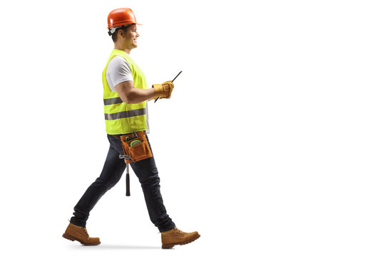 Full length profile shot of a construction worker with a helmet and tool belt holding a document and walking