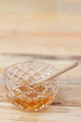 glass bowl with honey and honey dipper on a wooden table
