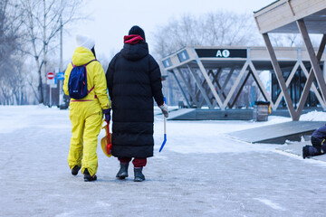 Fototapeta na wymiar Two young mothers wearing yellow and black winter coats walk past visitor centers in city park