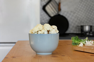 Fresh organic cauliflower cut into small pieces in ceramic bowl on wooden table in the kitchen. Healthy eating. Vitamins, antioxidants