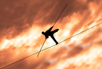 Wandering tightrope walker playing on yellow sky background. Silhouette of Equilibrist businessman with pole on the rope. idea concept of help and insurance, belay in business. Show in air.  - obrazy, fototapety, plakaty
