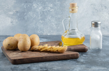 Sliced and whole potatoes on the cutting board with oil and salt