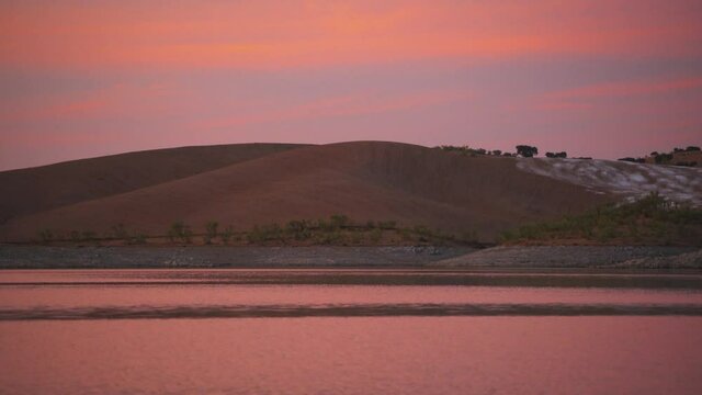 Desert like hill landscape with reflection on the water on a dam lake reservoir at sunset in Terena, Portugal