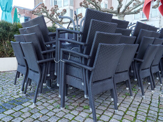 A stack of garden chairs and tables tied with a metal string. Beer garden closed in restaurant due to lockdown. Economic crisis. Chairs made of dark braided lines