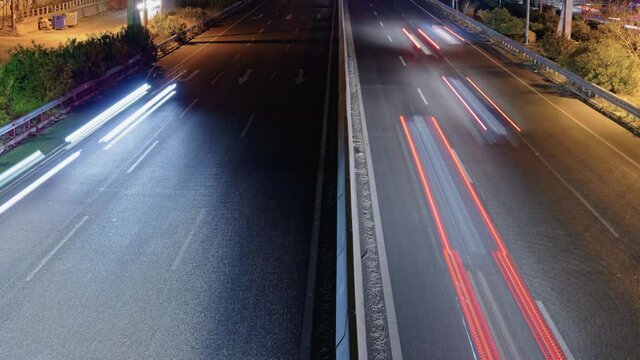 Elevated traffic time lapse on a highway separated by a median. Night top panorama of a European multi lanes road with passing cars leaving light trails in opposite directions in Thessaloniki, Greece.