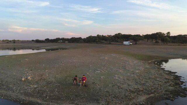 Caucasian couple sit on chairs on a lake drinking beer and seeing the landscape in Alentejo, Portugal