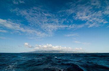Caribbean Island on the horizon.  Deep sea with waves view over blue sky with clouds and silhouette...
